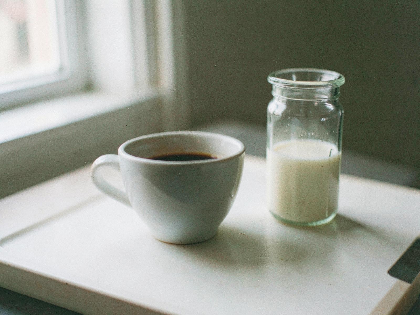 Tasse schwarzer Kaffee neben einem kleinen Milchkännchen am Fenster