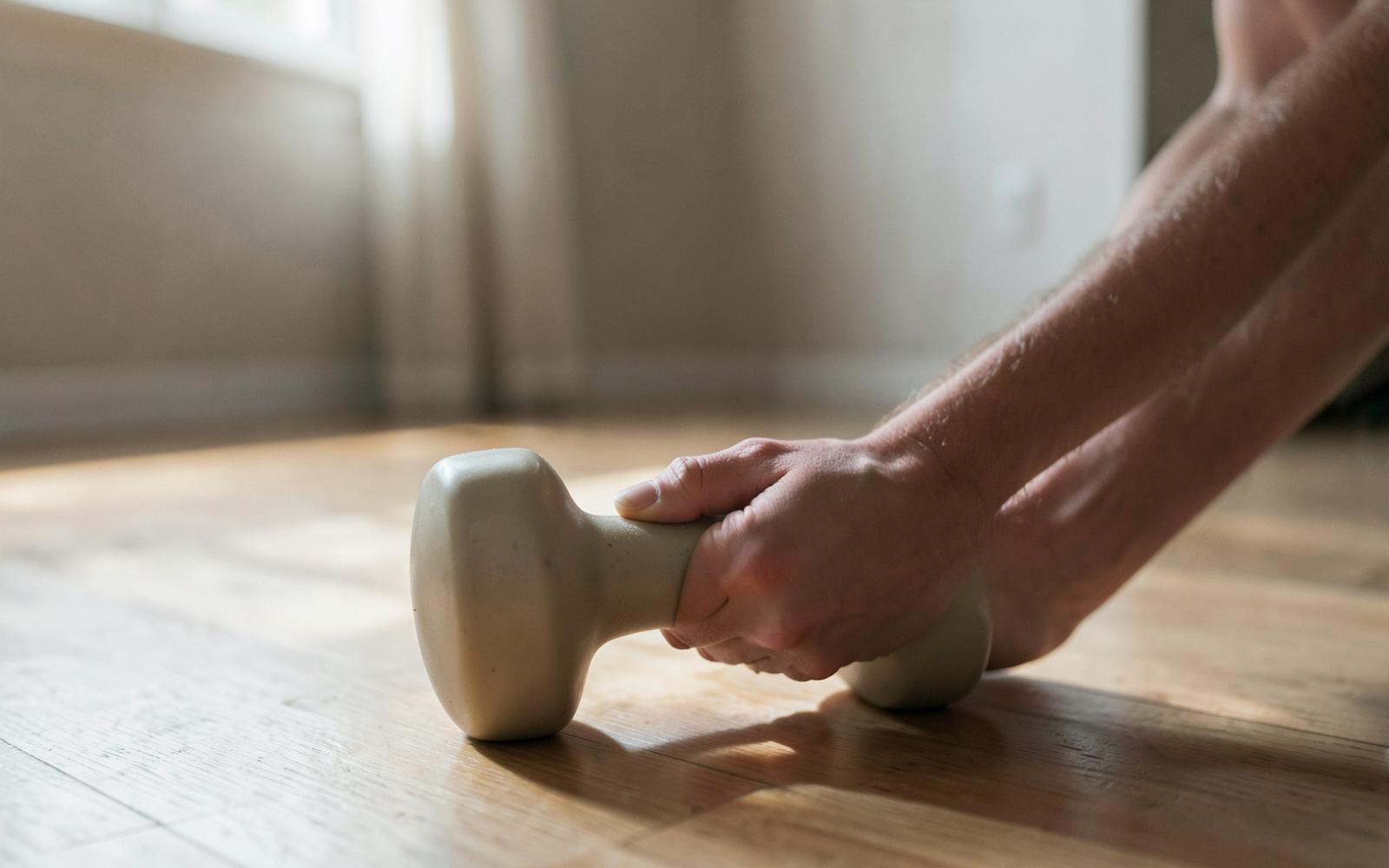 Hand an einer kleinen Hantel auf Holzboden im Tageslicht